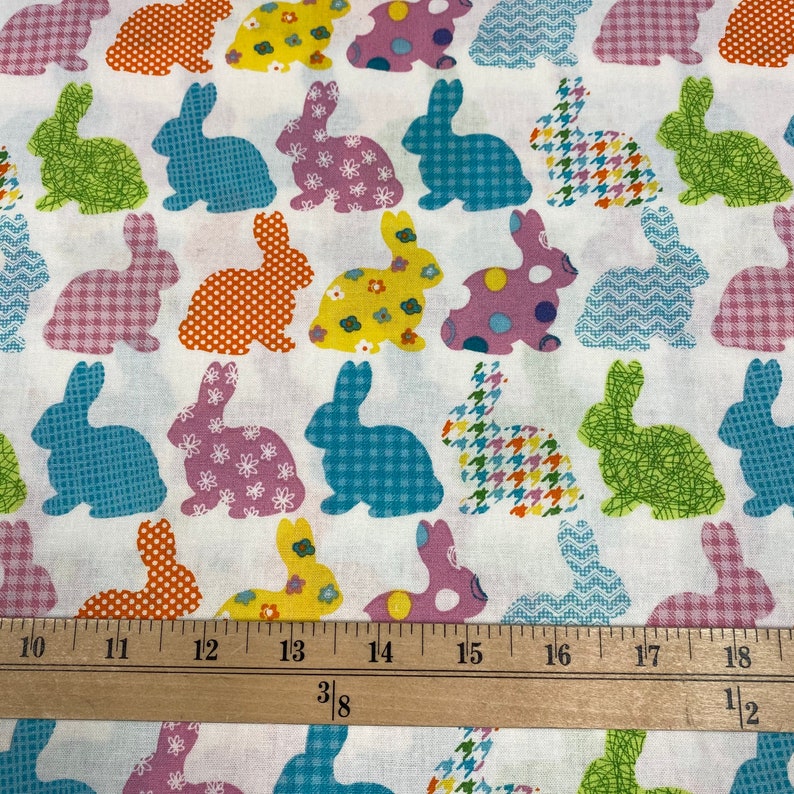 Puede incluir: Tela blanca con un patr&oacute;n repetido de siluetas de conejos de patchwork de colores. La tela se mide con una regla en pulgadas.