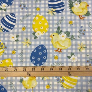 Puede incluir: Huevos de Pascua azules y amarillos y pollitos amarillos sobre un fondo de cuadros azules y blancos. Una regla de madera con marcas en pulgadas est&aacute; en la parte inferior de la imagen.