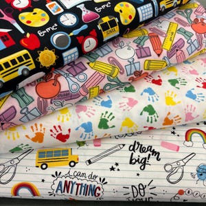 Könnte beinhalten: Stapel bunter Stoffe mit Schulmotiven. Designs umfassen Äpfel, Bleistifte, Scheren, Handabdrücke und die Texte "dream big!" und "I can do ANYTHING". Die Stoffe sind in Schwarz, Rosa, Weiß und anderen Farben.