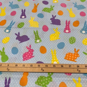 Puede incluir: Una tela azul con un patr&oacute;n repetido de conejos y huevos coloridos. Los conejos est&aacute;n en varias poses y colores, incluyendo rosa, verde, amarillo, naranja y morado. Los huevos tambi&eacute;n est&aacute;n en varios colores, incluyendo amarillo, naranja, verde y azul.