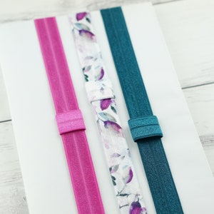 May include: Three hair ties, one pink, one teal, and one with a white background and a watercolour floral pattern.