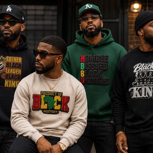 May include: A collection of four sweatshirts featuring graphic designs. One black hoodie displays 'FATHER BLACK LEADER BLACK KING', a beige sweatshirt reads 'PRODUCT OF BLACK HISTORY', a green hoodie says 'HUMBLE BLESSED BLACK UNBOTHERED', and a black sweatshirt says 'Black KING'.