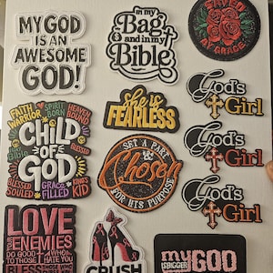 May include: A collection of embroidered patches with religious and inspirational themes. The patches feature phrases like "My God is Awesome God!", "Saved by Grace", and "Crush Cancer". Colors include black, white, pink, and gold.