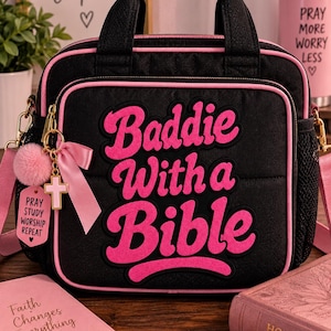 May include: A black quilted carrying case with pink piping and top handles. The front features the pink embroidered text "Baddie With a Bible". A pink pom-pom, a pink ribbon bow, and a cross charm hang from a gold-toned metal clip on the side.