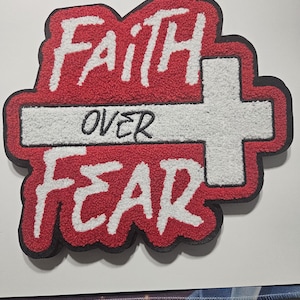 May include: A red and white patch with the words "Faith Over Fear" in a bold, textured font. The design includes a white cross and a black border, creating a striking visual statement.
