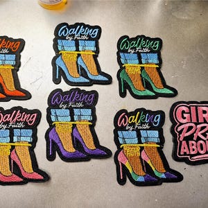 May include: A collection of seven embroidered patches. Six patches feature high-heeled shoes with blue jeans and the text Walking by Faith in various colors. One patch features the text GIRL, PRAY ABOUT IT! in pink with a black background.