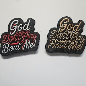 Peut inclure: Deux écussons brodés avec la phrase "God Don't Play Bout Me!". L'un a des lettres blanches et rouges, l'autre des lettres dorées. Les deux écussons ont une bordure noire et sont sur fond blanc.