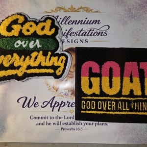 May include: Two embroidered patches. The left patch features yellow and green text reading God over Everything with a black background. The right rectangular patch has pink and yellow text reading GOAT and GOD OVER ALL THINGS.