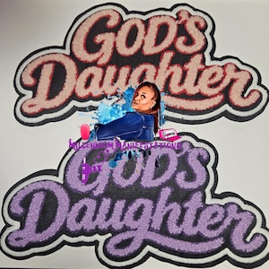 以下が含まれることがあります： God's Daughterという文字がテクスチャ感のあるふわふわした書体で刺繍された2つのワッペン。上のワッペンはライトピンク、下のワッペンはラベンダー色。その間には、青いジャケットを着て青いペンキを飛び散らせた人物のグラフィックが配置されている。