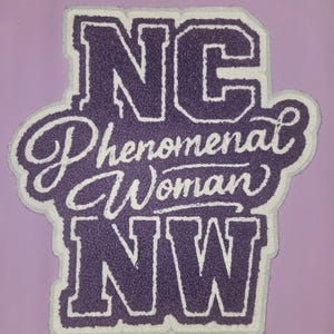 May include: A tufted rug featuring the purple text NC, Phenomenal Woman, and NW in a bold, blocky font for the initials and a cursive script for the middle phrase, all outlined in white against a solid purple background.