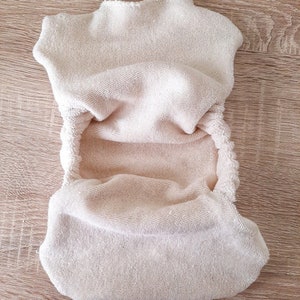 Könnte beinhalten: Eine beige Stoffwindel aus weichem, saugfähigem Frottee. Die Windel ist in der Hälfte gefaltet und einsatzbereit.