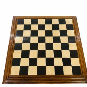 Puede incluir: Un tablero de ajedrez de madera con un patrón de tablero de ajedrez negro y marrón claro. El tablero tiene un marco de madera marrón oscuro con un doble borde.