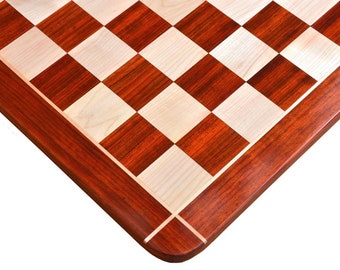 May include: A close-up of a wooden chessboard with a checkerboard pattern. The squares alternate between light wood and dark reddish-brown wood. The board has a dark reddish-brown border.