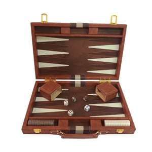 May include: Open brown leather backgammon set with a light beige playing surface. The set includes dice, dice cups, and game pieces. The case has a handle and gold-colored hardware. The game is open and ready to play.