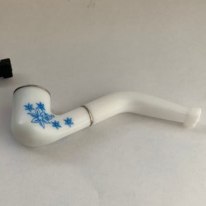 May include: White ceramic pipe with a blue floral design. The pipe has a curved stem and a round bowl.