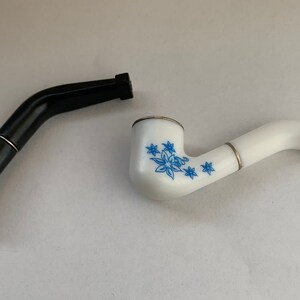 May include: Two smoking pipes, one black and one white with a blue floral design.