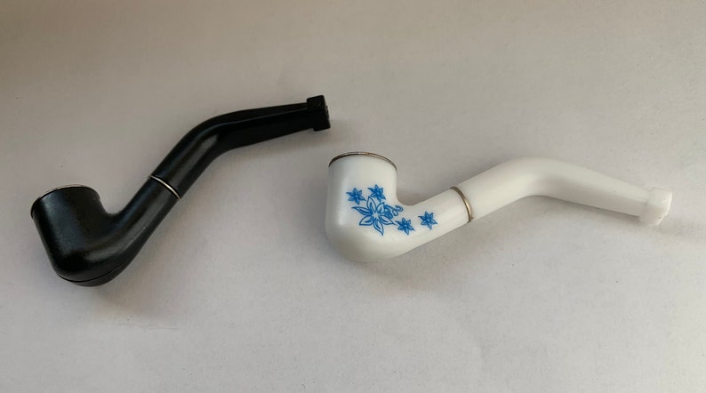 May include: Two smoking pipes, one black and one white with a blue floral design.