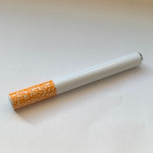 May include: A white and orange cigarette-shaped pipe with a white and orange patterned design.