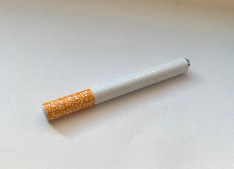 May include: A white and orange cigarette-shaped pipe with a white and orange patterned design.
