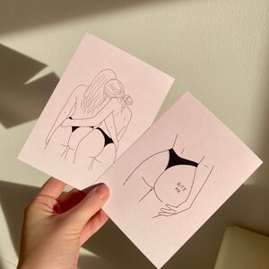 May include: Two line drawings of female figures in black and white. The first image shows two figures embracing. The second image shows a single figure with the text "Bite Me" written on the hip.