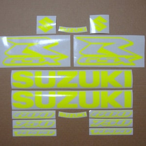 Puede incluir: Un conjunto de calcomanías de motocicleta amarillas con el logotipo de Suzuki y el texto "GSXR" y "600 750 1000".
