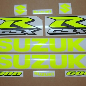 Puede incluir: Un conjunto de calcomanías para motocicleta de color amarillo y negro con el texto "GSX" y "600" y la palabra "SUZUKI" repetida dos veces.