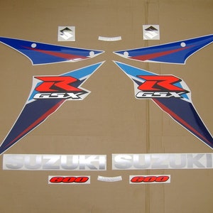 Puede incluir: Un conjunto de calcomanías para motocicleta con un esquema de color azul, rojo y blanco. Las calcomanías incluyen el logotipo de Suzuki, el texto "GSX" y el número "600".