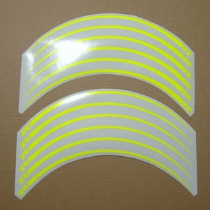 May include: Two curved, white decals with multiple horizontal, neon yellow stripes. The decals have a slight arc shape, and a small section of text is visible on the right side of each decal. These are likely for vehicle customization.
