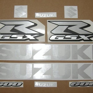 Puede incluir: Un conjunto de calcomanías de motocicleta plateadas y negras con las palabras "Suzuki" y "GSX 600" impresas en ellas.