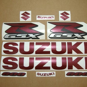 Puede incluir: Calcomanías de motocicleta de color rojo burdeos y plata con el texto "GSX 600" y "SUZUKI".