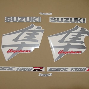 May include: A set of silver and red motorcycle decals with the words "Suzuki", "Hayabusa", and "GSX 1300 R".