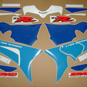 Puede incluir: Un conjunto de calcomanías para motocicleta de color azul, blanco y rojo con el texto "Suzuki", "V-Twin Superbike" y "SRAD Suzuki Ram Air Direct".