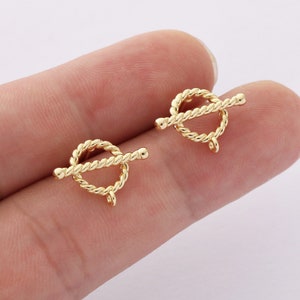 May include: Two gold-toned metal toggle clasps with a rope-like design. The clasps are circular with a bar that slides through the circle.