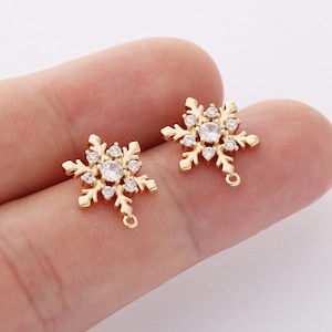 May include: Two gold-tone snowflake charms with clear crystal accents. Each charm has a loop for attaching to jewelry or other crafts.