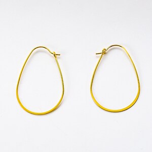 May include: A pair of gold oval hoop earrings. The earrings are made of thin wire and have a simple, elegant design.