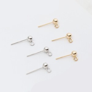 May include: A collection of stud earrings in gold and silver tones. Each earring features a small ball at the top of a straight post, with a small loop attached. The earrings are displayed against a white background.