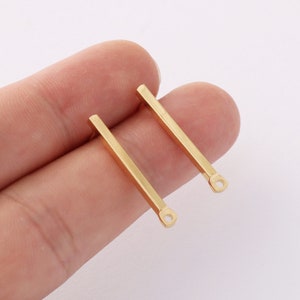 May include: Two gold-coloured metal earring posts with a straight bar design and a small loop at the end.
