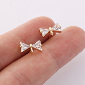 May include: A pair of gold bow-shaped earrings with clear cubic zirconia stones.