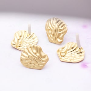 May include: Four gold-coloured metal earring findings with a textured surface. Each finding has a small loop and a post for attaching an earring.