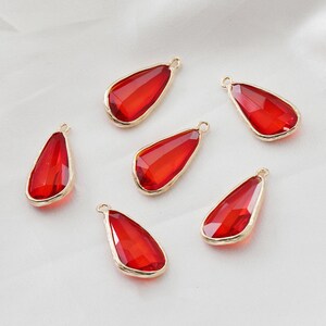 Könnte beinhalten: Sechs rote tropfenförmige Glasanhänger mit goldfarbenen Metallakzenten. Die Anhänger haben ein facettierten Design und sind perfekt für die Schmuckherstellung.