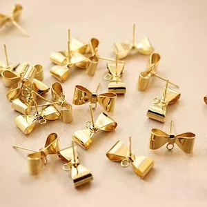 May include: A group of 18 gold-tone bow-shaped earring findings. The findings are made of metal and have a post and a loop for attaching earrings.