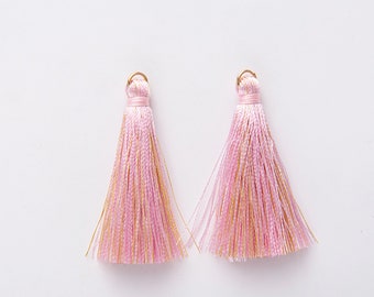 May include: Two pink and gold tassel charms with a gold loop at the top.