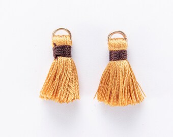 May include: Two small gold tassel charms with brown trim. The tassels are made of a soft, yellow fabric.