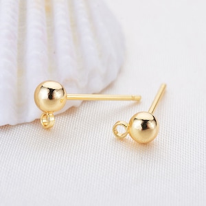 May include: Two gold-toned earring posts with a small loop at the bottom and a round ball at the top.