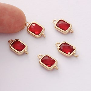 May include: Five gold-toned metal charms with red glass square-shaped stones. Each charm has a loop on either side.