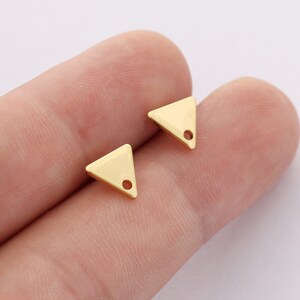 May include: Two gold triangle shaped earring charms with a small hole at the top.