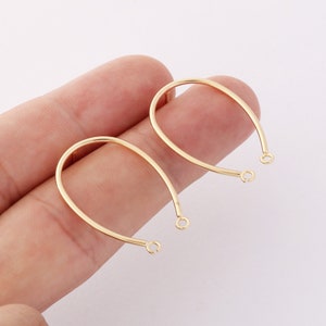 May include: Two gold-coloured, U-shaped earring components. Each component has a curved top and straight bottom with a small loop at each end. The earrings are made of a shiny, metallic material and are displayed against a light background.