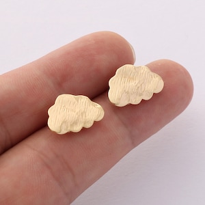 May include: A pair of gold-tone cloud-shaped earrings. The earrings are small and delicate, and they have a textured surface.