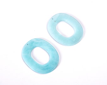May include: Two oval-shaped, light blue acrylic pendants with a marbled effect. Each pendant has a small hole at the top for stringing. The pendants are set against a white background.