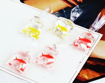 Könnte beinhalten: Fünf transparente Plastiktüten mit einem goldenen oder roten Fisch darin. Die Tüten hängen an einer weißen Oberfläche. "POST CARD" steht auf der Oberfläche.